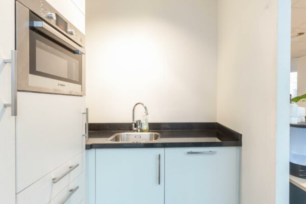 Kleine kitchenette met een ingebouwde Bosch oven, rvs-spoelbak en wit aanrechtblad in een modern interieur aan de 1e Hogeweg.